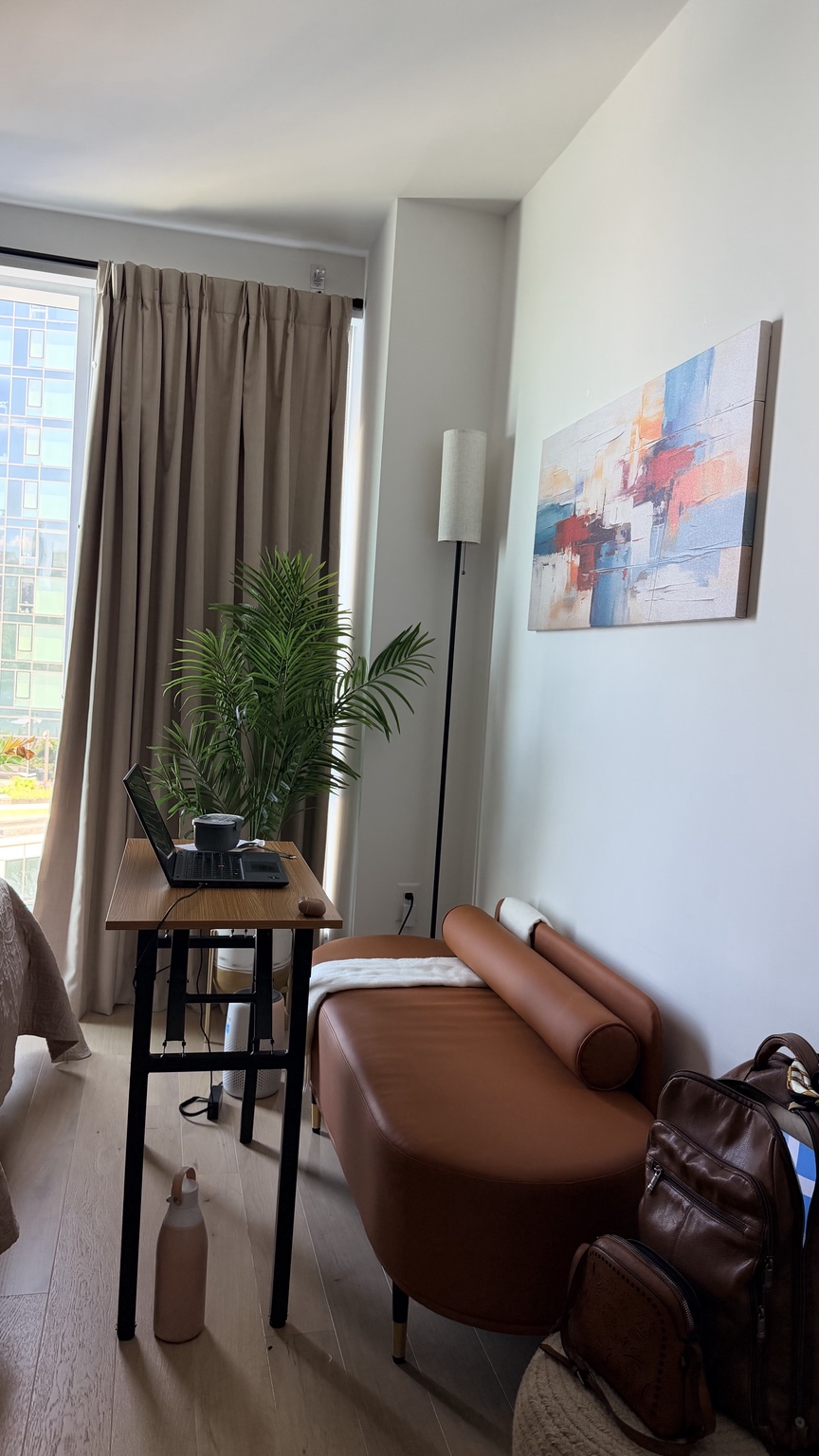 A quiet writing space — wooden desk, tan daybed, plant by the window