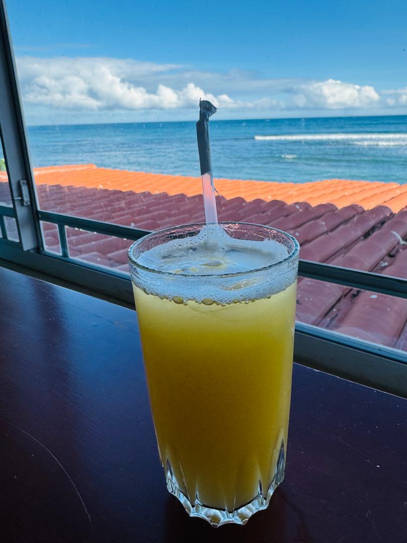 A glass of orange juice on a wooden table overlooking the ocean